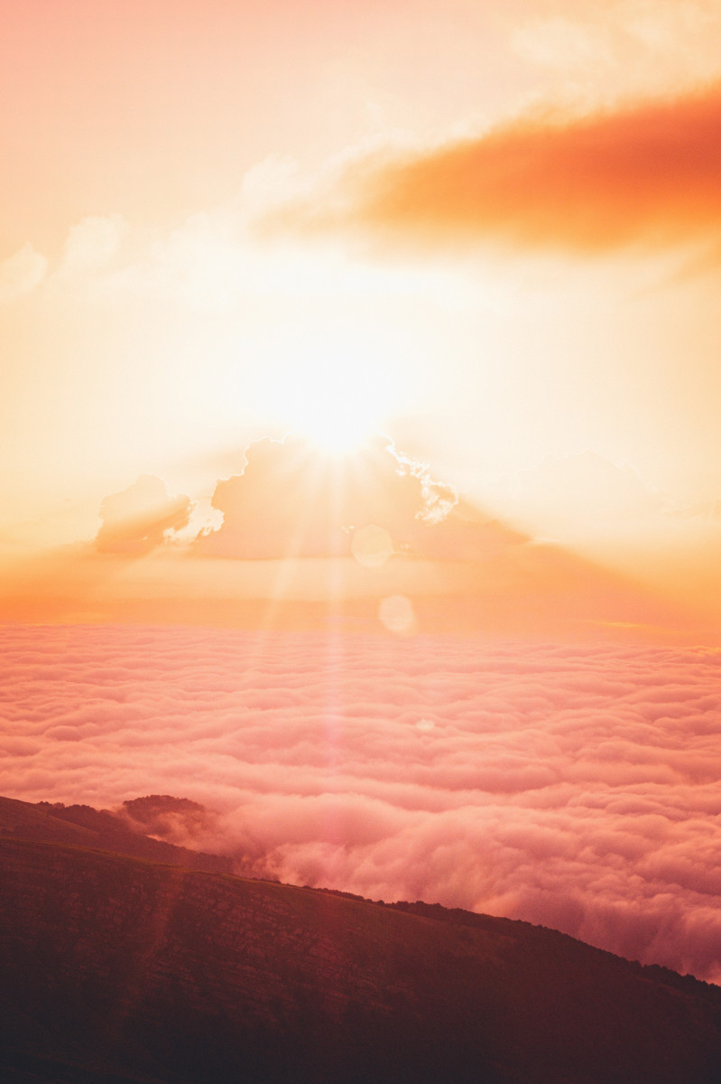 The sun shining on top of rolling clouds