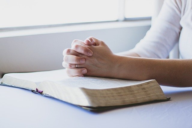 Hands clasped in prayer on top of a Bible