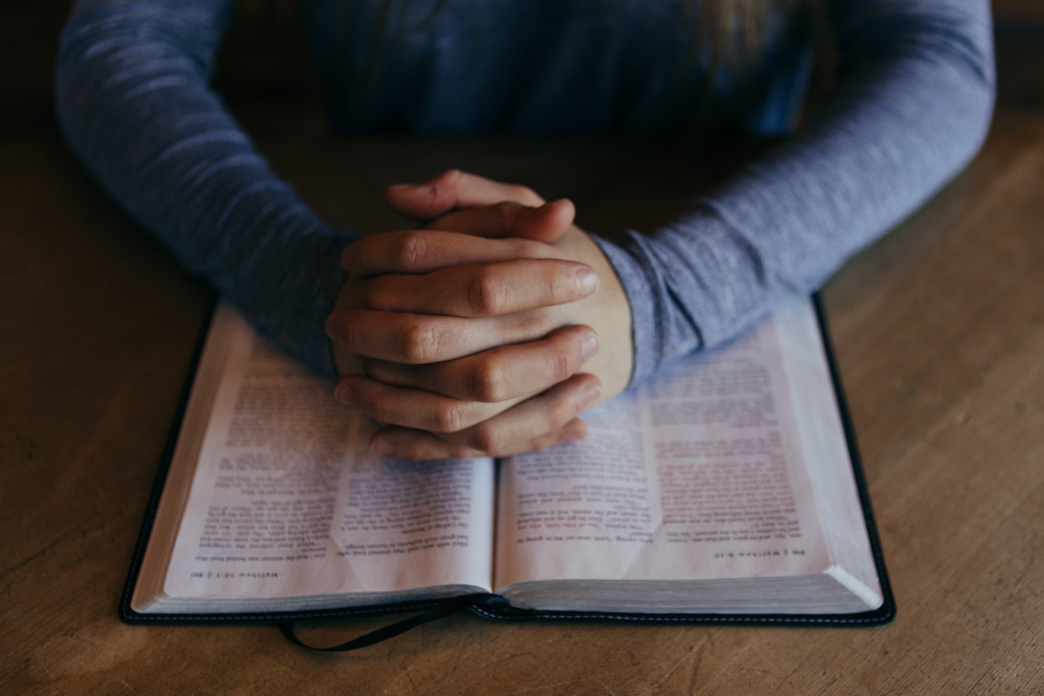 Hands clasped on top of an open book