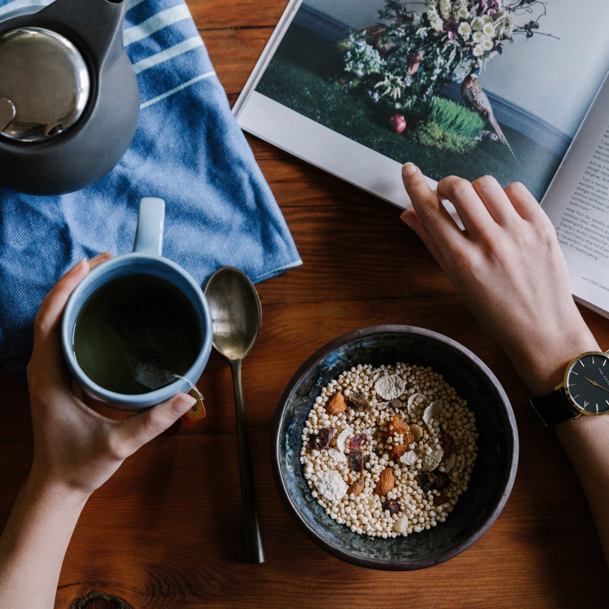 A person eating breakfast with a cup of tea and a book